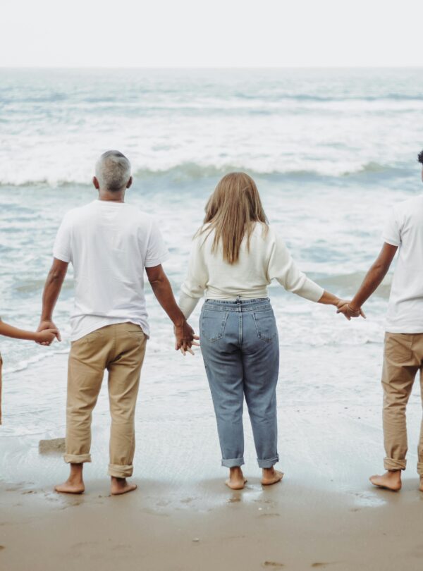 A family of four holds hands while facing the ocean, enjoying a peaceful day at the beach.
