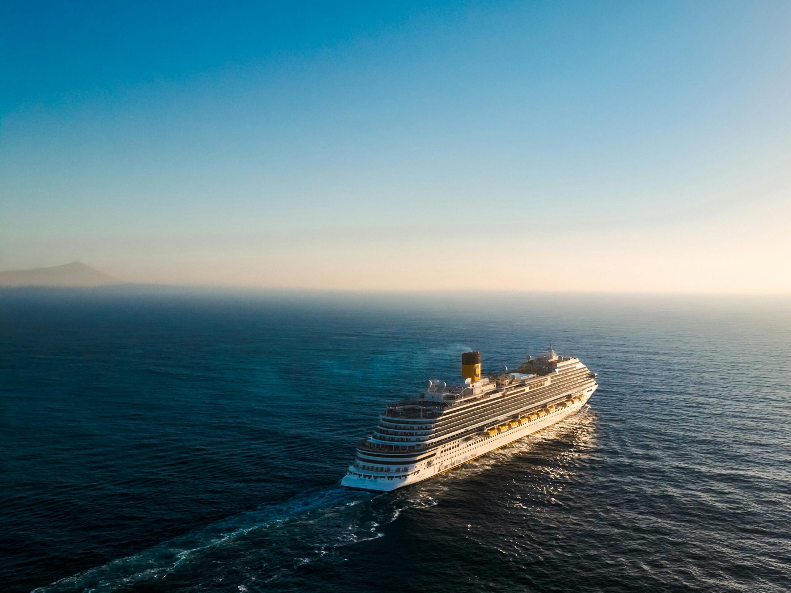 Aerial view of a luxury cruise ship navigating the calm ocean waters during sunset.