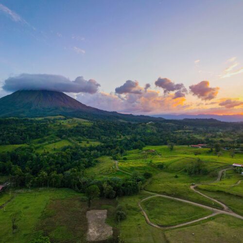 Breathtaking aerial view of Arenal Volcano at sunset in Alajuela Province, highlighting lush landscapes.