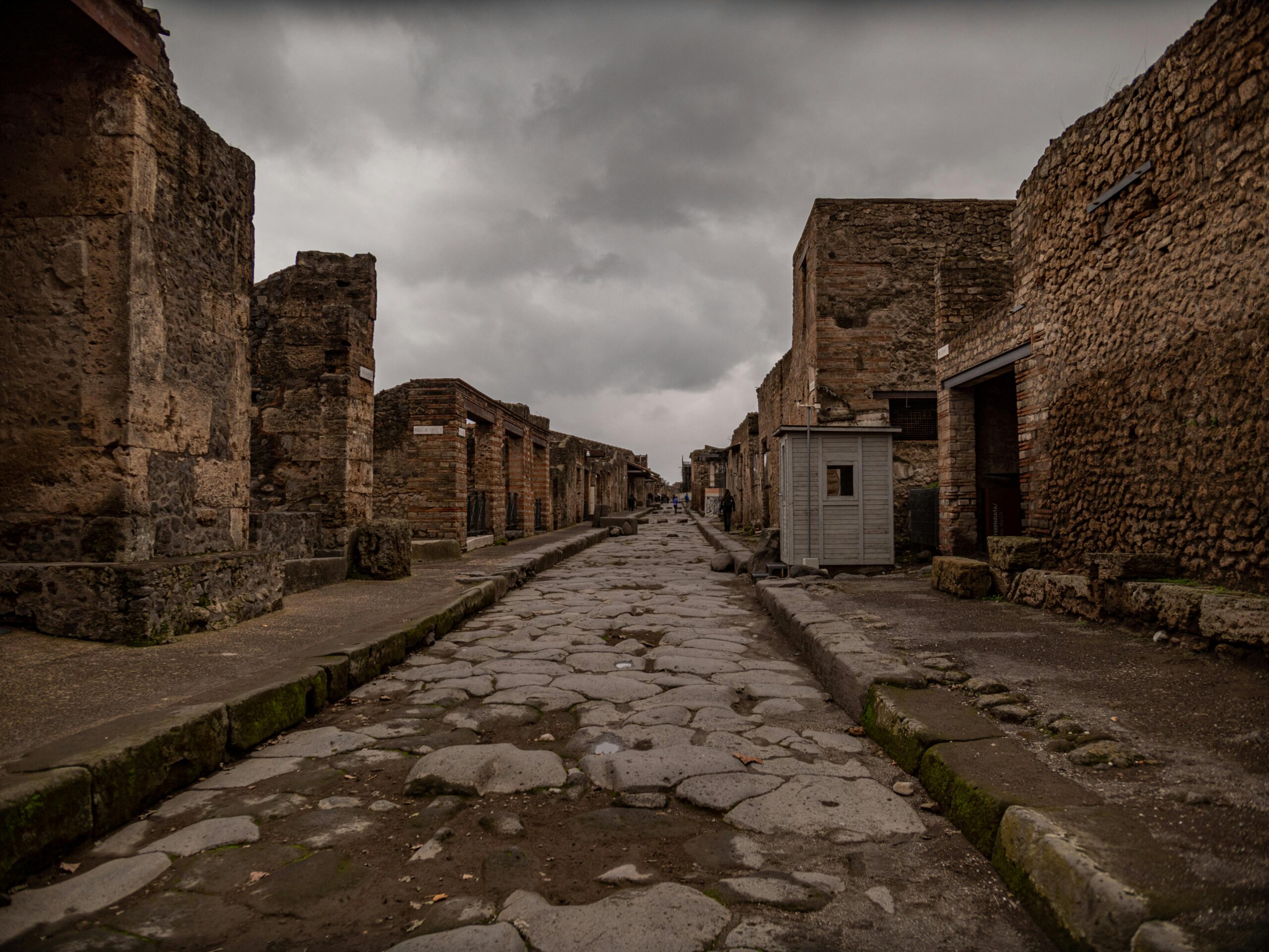 A deserted ancient street in Pompeii, Italy, with historic ruins and an overcast sky.
