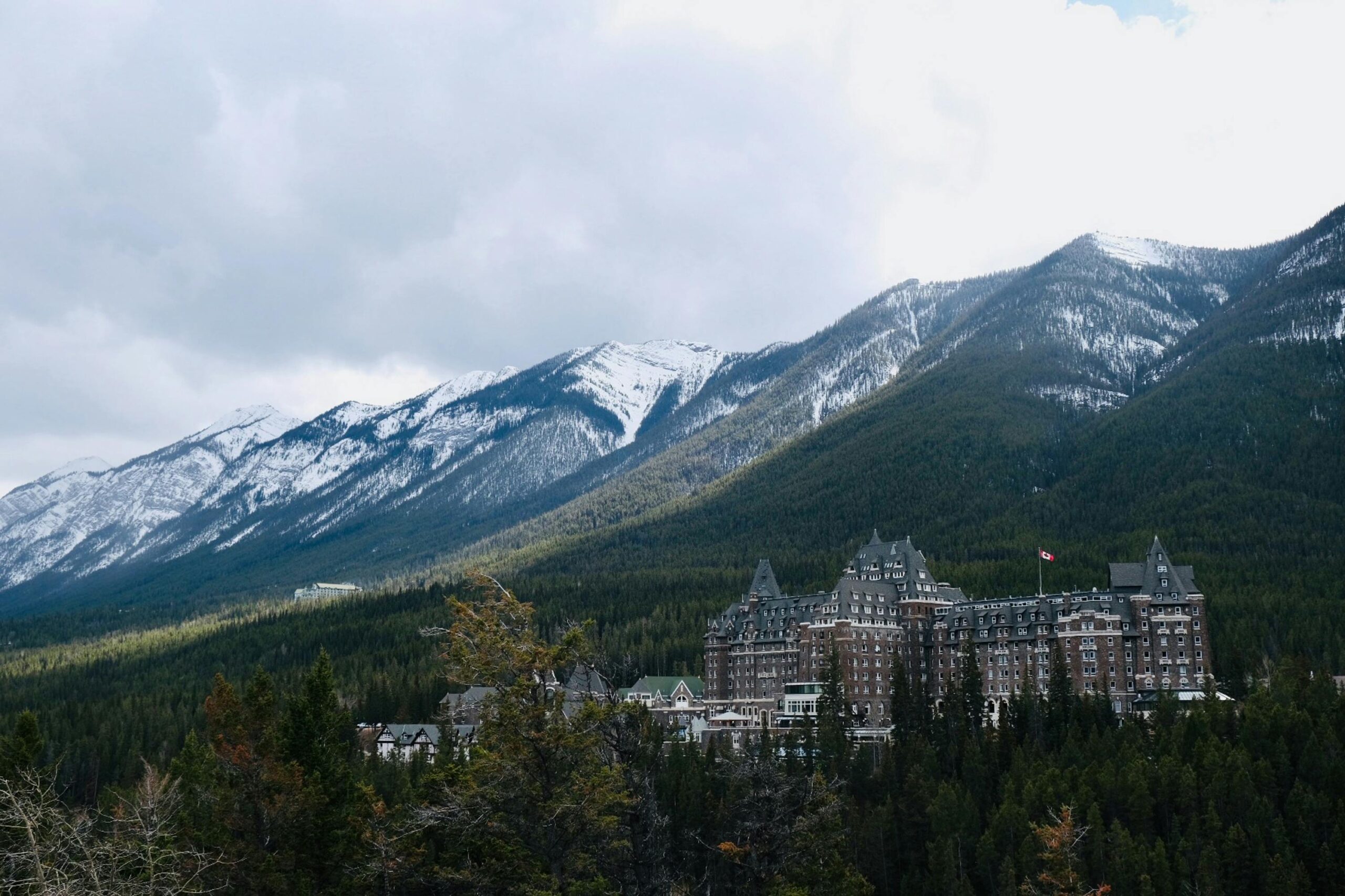 Scenic view of Banff Springs Hotel amidst snow-capped mountains and greenery.