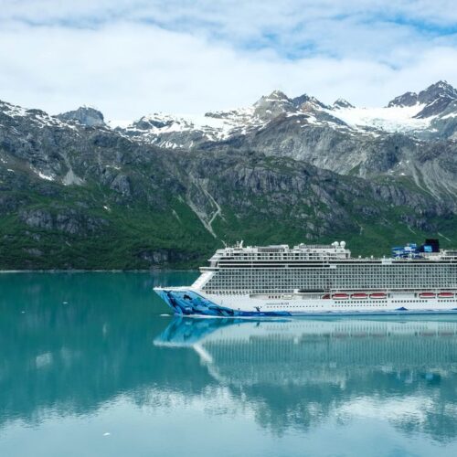 A majestic cruise ship sailing through clear waters with snowy mountains as a backdrop.