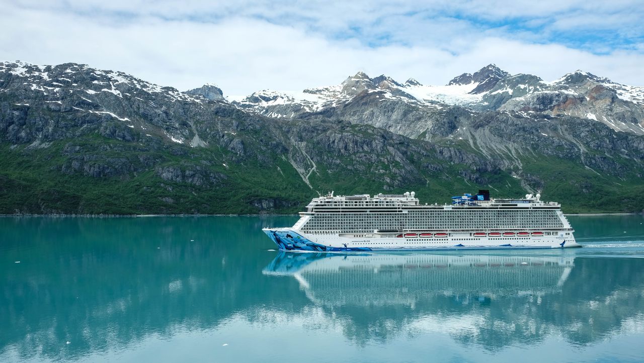 A majestic cruise ship sailing through clear waters with snowy mountains as a backdrop.